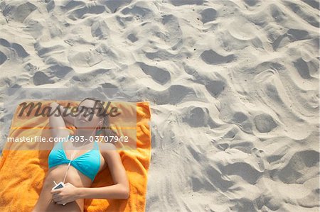 Teenage girl (16-17) using mp3 player, lying on beach, view from above