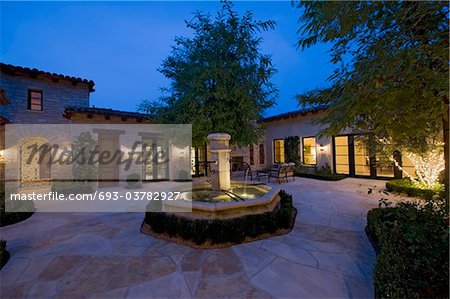 House exterior at night with a fountain,patio furniture and trees,one in which is lit with fairy lights