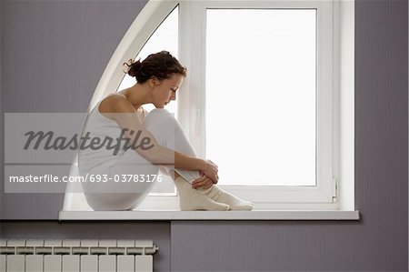 Mid Adult Woman Sits On Windowsill With Ankles Crossed Stock