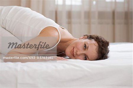 Mid adult woman kneels on bed smiling at camera