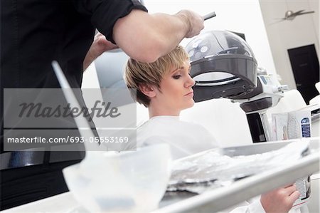 Woman Reading Magazine While Hairdresser Coloring Hair Stock