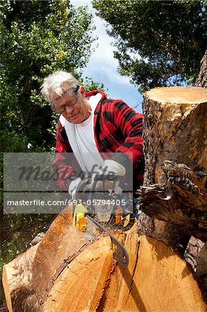 Senior man cutting tree stump with chainsaw