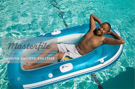 Boy (13-15) Relaxing on Inflatable Raft in swimming pool, elevated view.