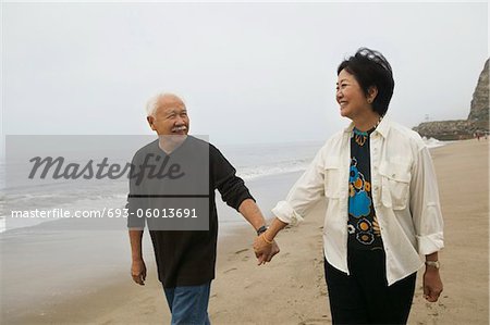 Mature couple holding hands, walking on beach