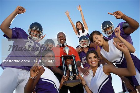 Football coach, players and cheerleaders holding trophy outside, low angle view, portrait, (portrait)