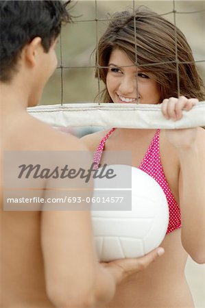 Couple Flirting by Volleyball Net, man holding ball