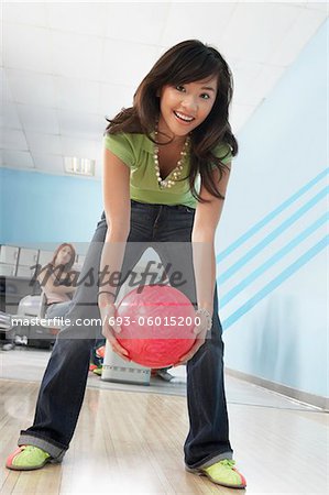 Young woman at bowling alley holding ball, portrait