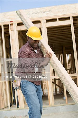 Construction worker carrying wooden plank