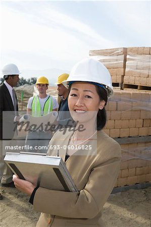 Two architects standing on construction site holding blueprints