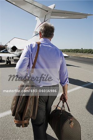 Senior businessman going towards airplane on landing strip.