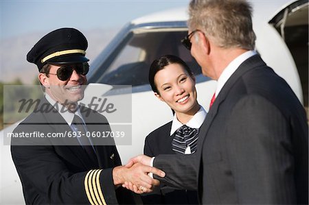 Mid-adult airline pilot and senior businessman shaking hands.