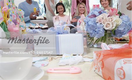Friends at baby shower sitting behind gifts and flowers
