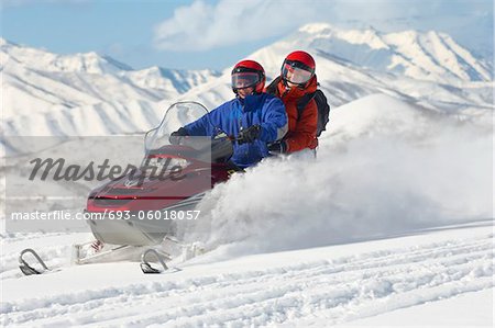 Couple driving snowmobile in front of snow covered mountains