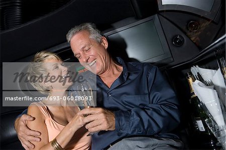 Middle-aged couple sitting on back seat of limousine and drinking champagne
