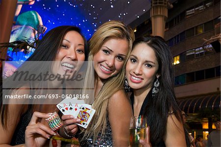 Portrait of three young women with playing cards, gambling chips and champagne in front of casino, Las Vegas, Nevada, USA
