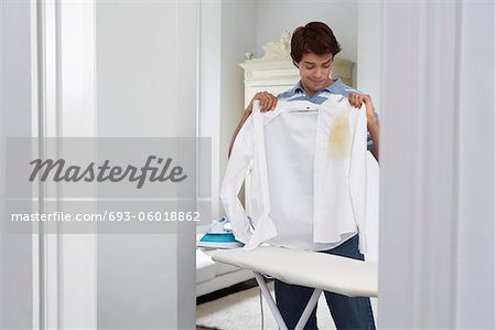 Man holding burned shirt by ironing board