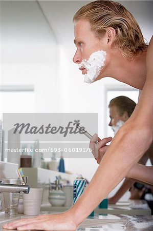Man shaving face in bathroom