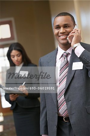 Business man using mobile phone with business woman writing in diary in background