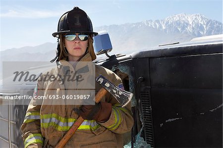 Portrait of female firefighter holding axe in mountains