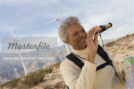 Mature woman with binoculars by wind farm