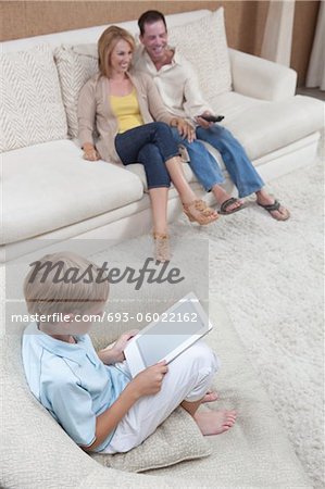 Parents watch television while son reads a digital book