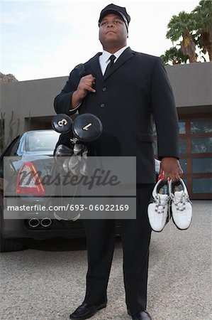 Chauffeur stands with golf equipment near luxury vehicle