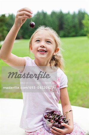Happy young girl holding bowl full of bing cherries in park