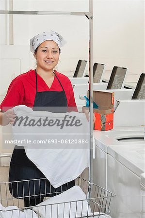 Portrait of a happy woman wearing uniform holding clothes with washing machines in background