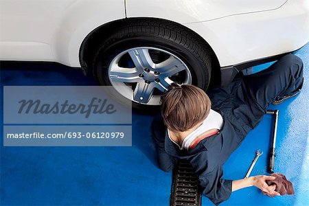 High angle view of woman lying on floor working on car in workshop