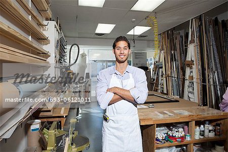 Portrait of a happy young craftsman standing with arms crossed in workshop
