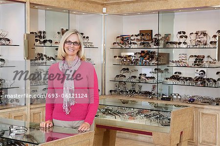 Portrait of a happy senior female optician standing in store