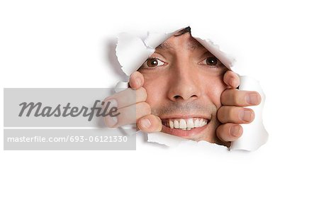 Portrait of a happy young Hispanic man peeking from ripped paper hole