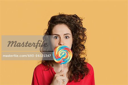Portrait of a young woman holding lollipop in front of face over colored background
