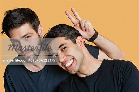 Portrait of young male friends with peace sign over colored background