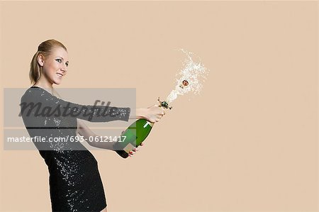 Beautiful young woman uncorking champagne bottle over colored background