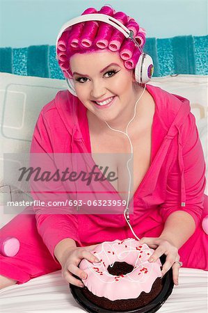 Portrait of a happy young woman wearing headphones sitting on bed with cake