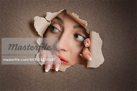 Young Middle eastern woman looking away from ripped paper hole
