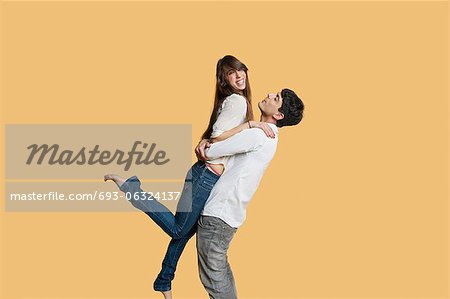 Happy young man carrying girlfriend over colored background