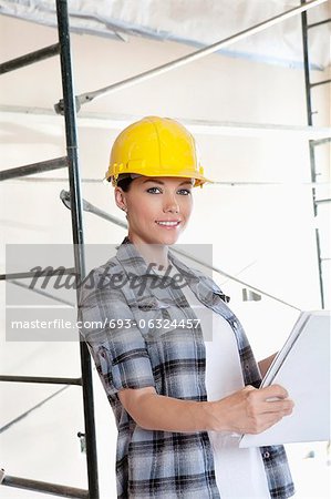 Portrait of beautiful mid adult architect wearing hardhat with blueprints