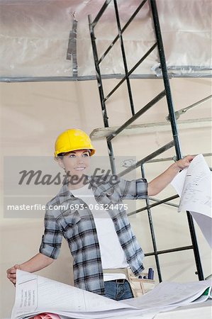 Happy mid adult worker holding building plans while looking away