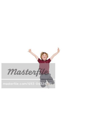 Portrait of elementary boy jumping in air with arms raised over white background