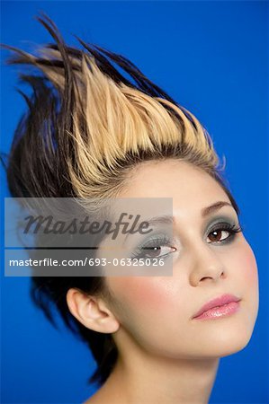 Close-up portrait of beautiful young woman with spiked hair over blue background