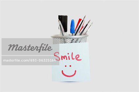 Close-up of adhesive notepaper with smiley face stuck on pen holder over white background