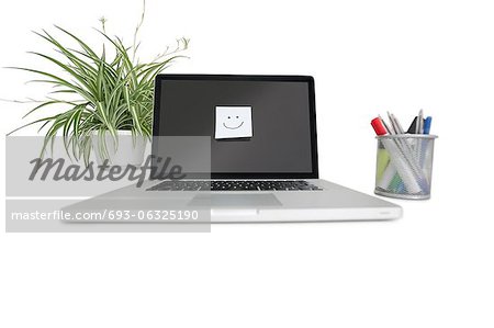 Smiley face sticky note on laptop with office supplies and pot plant