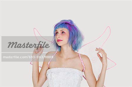 Beautiful young woman dressed as angel with dyed hair looking up against gray background