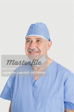 Happy senior male surgeon with surgical mask and cap over gray background
