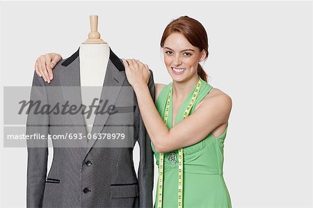 Portrait of beautiful female dressmaker standing with tailor's dummy over gray background