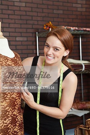 Portrait of happy female fashion designer standing by tailor's dummy with cloth on it