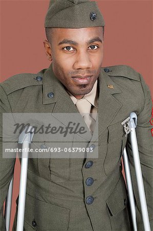 Portrait of African American military officer with crutches, studio shot on brown background