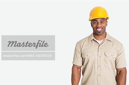 Portrait of happy young African man wearing yellow hard hat helmet over gray background